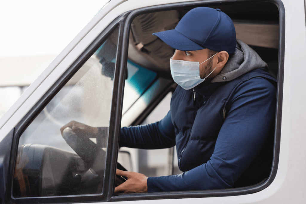 Close up of a truck driver leaning out the window of a semi truck while wearing a face mask