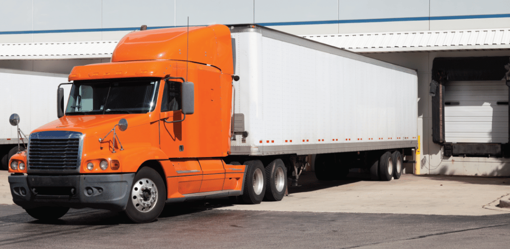 an orange semi truck sits in a loading dock