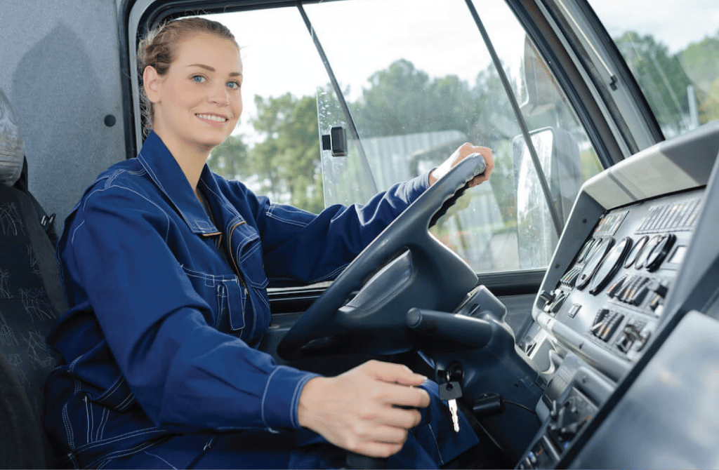a smiling female truck driver sits in the drivers seat reaching for the ignition