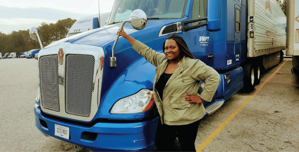 A smiling woman poses next to a blue semi truck