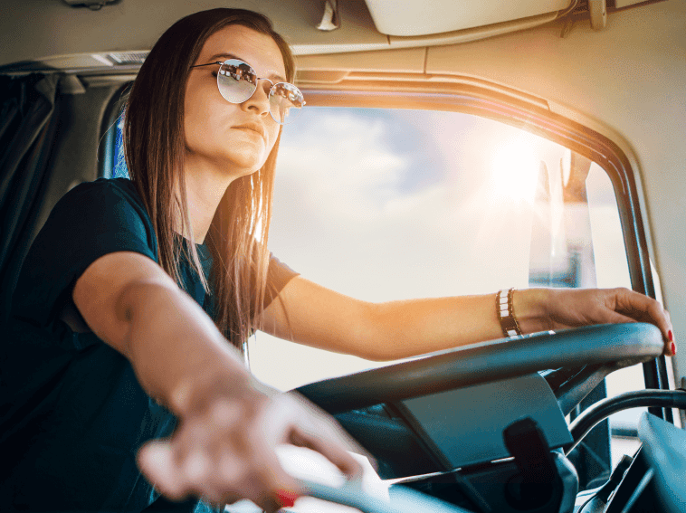 female trucker on the road with one hang on the steering wheel and one on the ignition