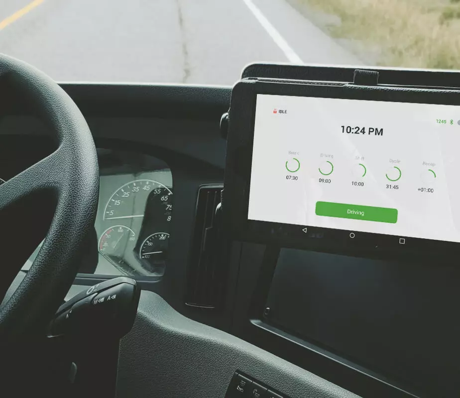 steering wheel and the GPSTab ELD are displayed on the dashboard of a truck and the windshield reveals that the truck is driving down the road.