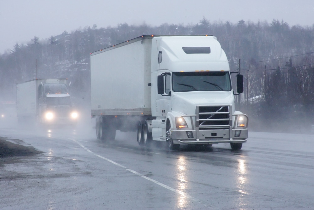 A white semi truck driving down a highway in the rain